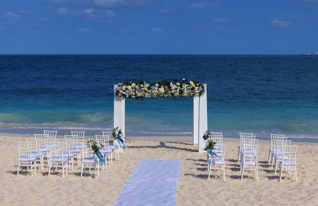 Beach wedding ceremony in white with greenery and blue and white flowers at a beach resort in costa mujeres