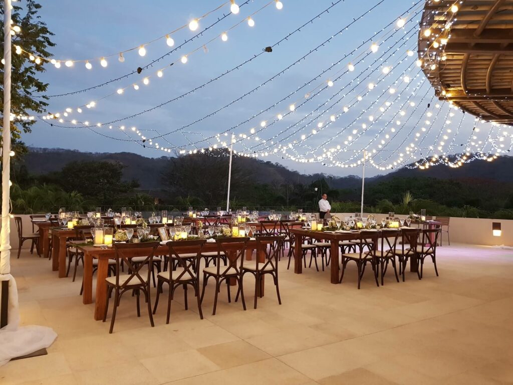 rooftop area set for a wedding reception with string lights and crossback wooden chairs