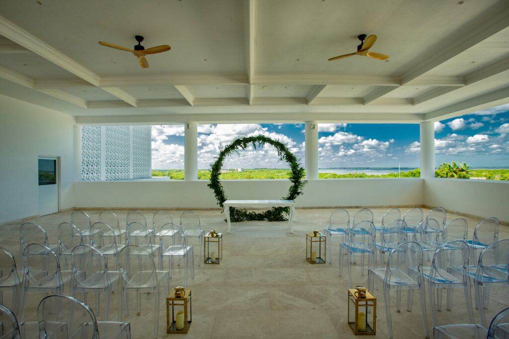 Destination wedding ceremony set-up with ghost chairs and circle ceremony arch with greenery at the Wedding Ballroom Terrace of the Majestic Elegance Costa Mujeres