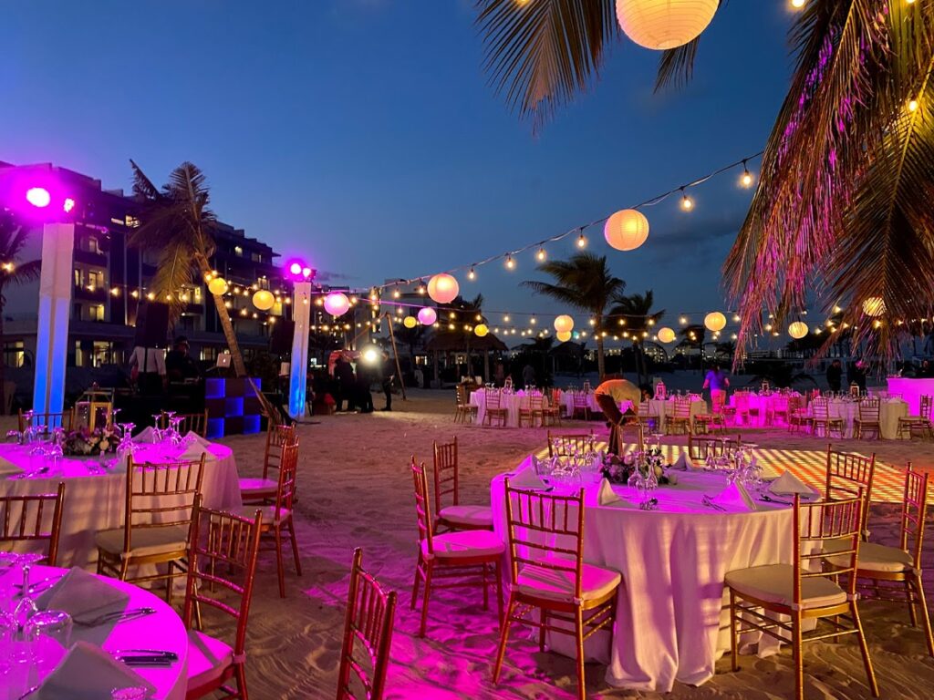Destination wedding beach reception with infinity chair, round table with white linen and string lights at the Majestic Elegance Costa Mujeres