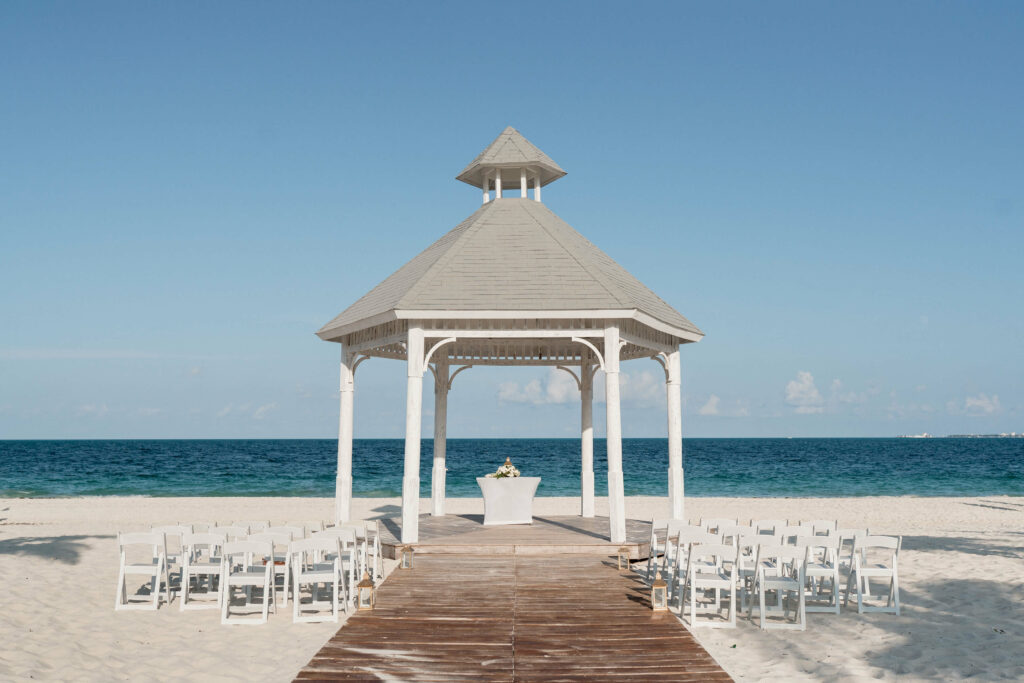 Destination wedding ceremony with white foldable chairs, wooden aisle at the beach gazebo of the Majestic Elegance Costa Mujeres