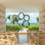 Stone wedding gazebo with ocean view and flower garlands and wooden chairs