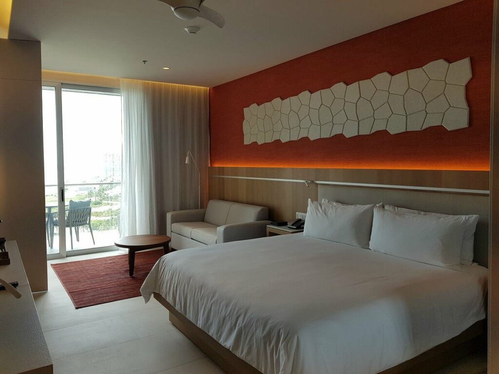 hotel room interior with king bed, white bedding and orange wall
