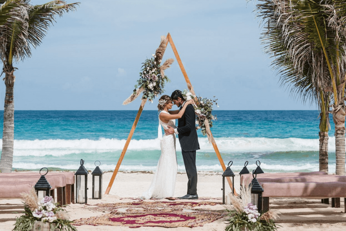 Couple getting married at Live Aqua Cancun under a flower arrangement with the sea behind them