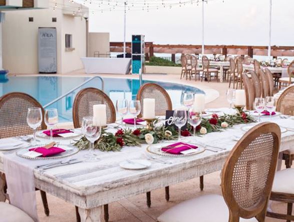 Destination Wedding reception set-up with rectangular table, cane back chair and natural flower table runner at the pool club of Live Aqua Cancun