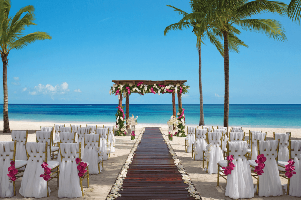 Beach gazebo set up for a wedding with pink flowers and golden chairs