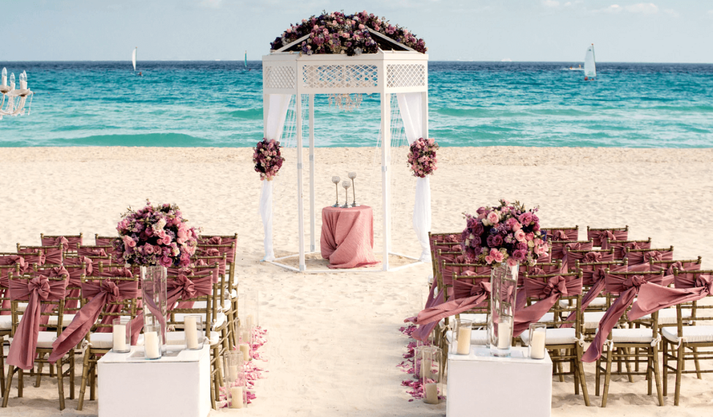 Beach wedding gazebo with golden chairs and pink ribbons and flowers