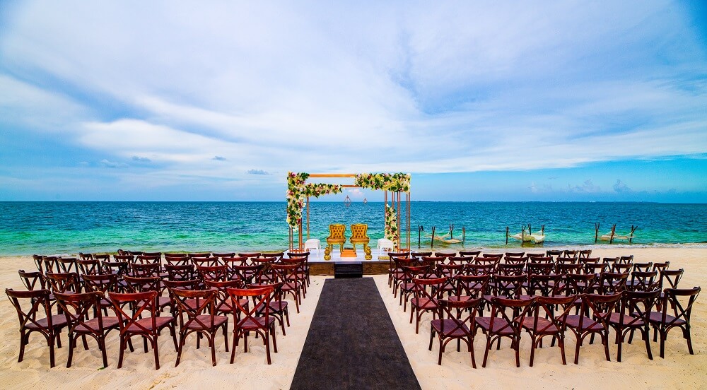 Destination wedding beach ceremony set--up with wooden pergola and tifany chairs at Atelier Playa Mujeres