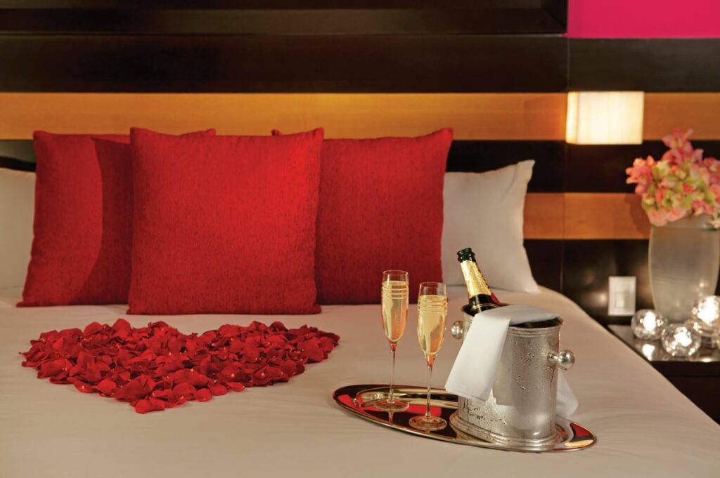 Romantic bed arrangement with red rose petals and two glasses of champagne on the bed