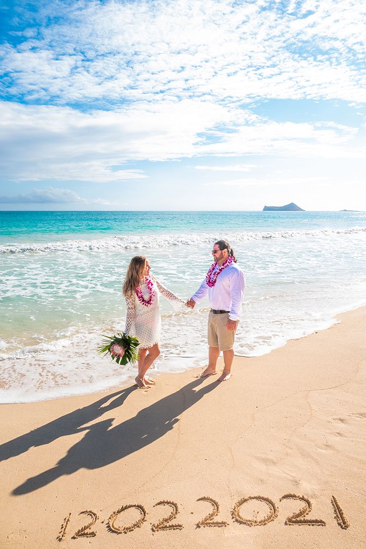 Married couple holding hands on the beach with purlpe orchid lei necklaces orchid