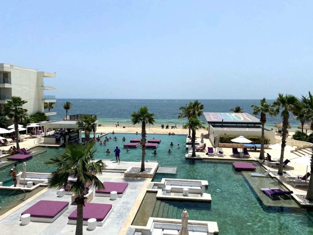 Aerial view of the hotel pool in front of the beach with large purple cushions