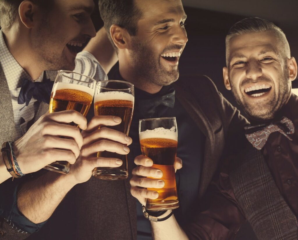 Three male friends holding each other, laughing and toasting with beers