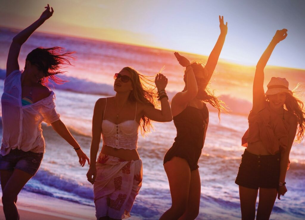 Four girlfriends dancing at the beach during sunset