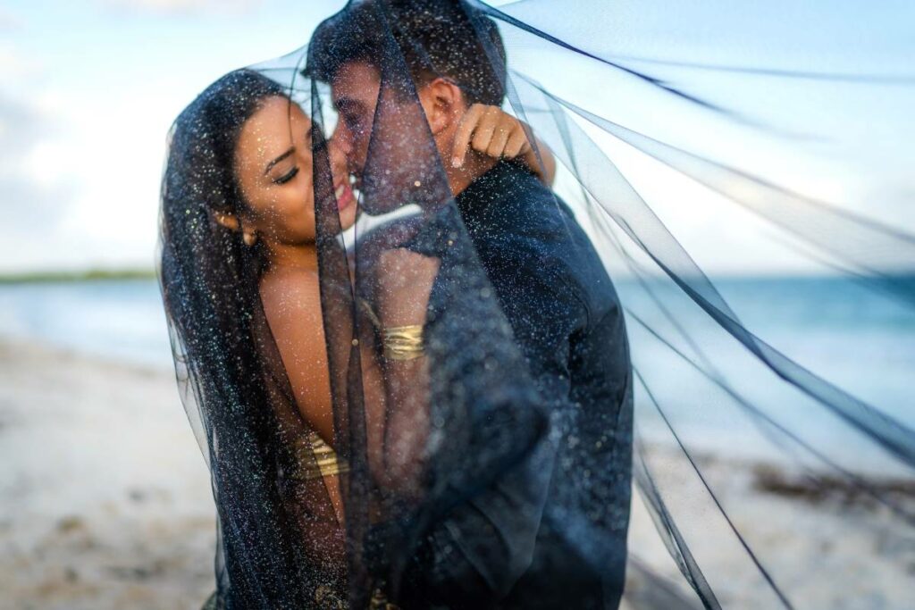 Elopement couple kissing on a beach under a veil