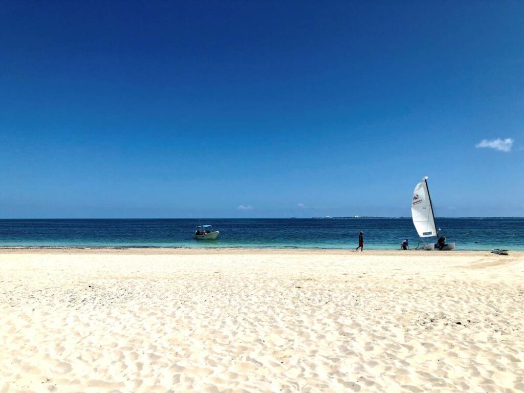 Expansive clear beach with a small boat and a windsurfing board