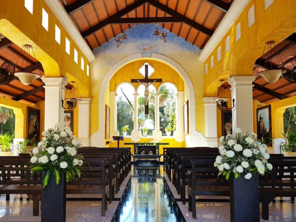 Spanish colonial open chappel with bright yellow colors, paintings of saints and white flower arrangements