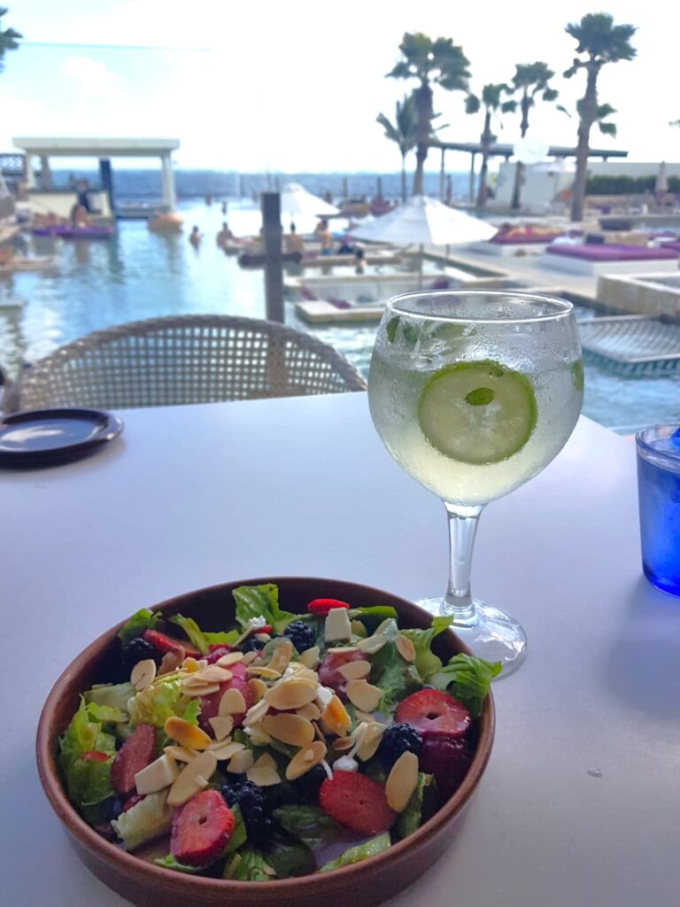 Salad bowl with red berries and a gin tonic, with a view of the pool