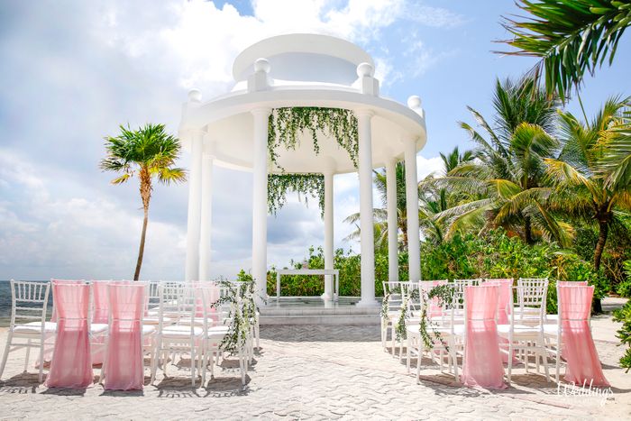 Oceanfront wedding gazebo with white chairs, pink drapes and greenery