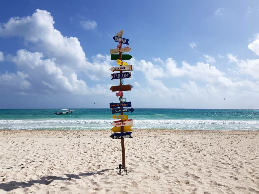 Expansive and beautiful caribbean beach with sings pointing towards major cities