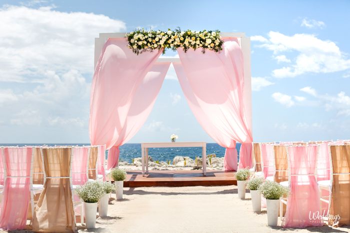 Belvédère de mariage en bord de mer avec rideaux roses et fleurs blanches