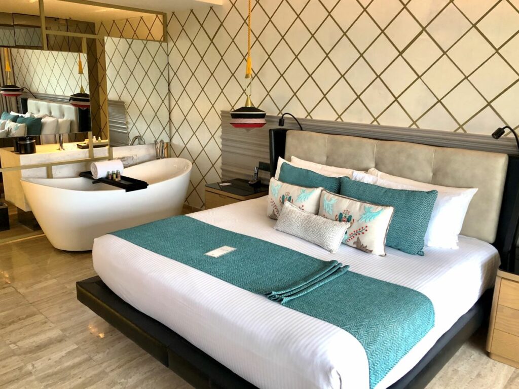 Chambre d'hôtel avec meubles en bois, tissus bleus, grands miroirs et baignoire
