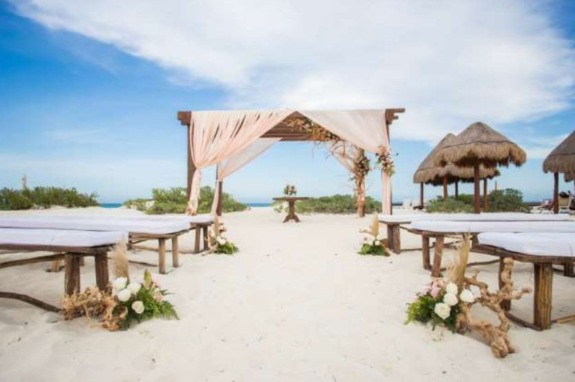 Beach wedding gazebo with pink drapes and wooden benches