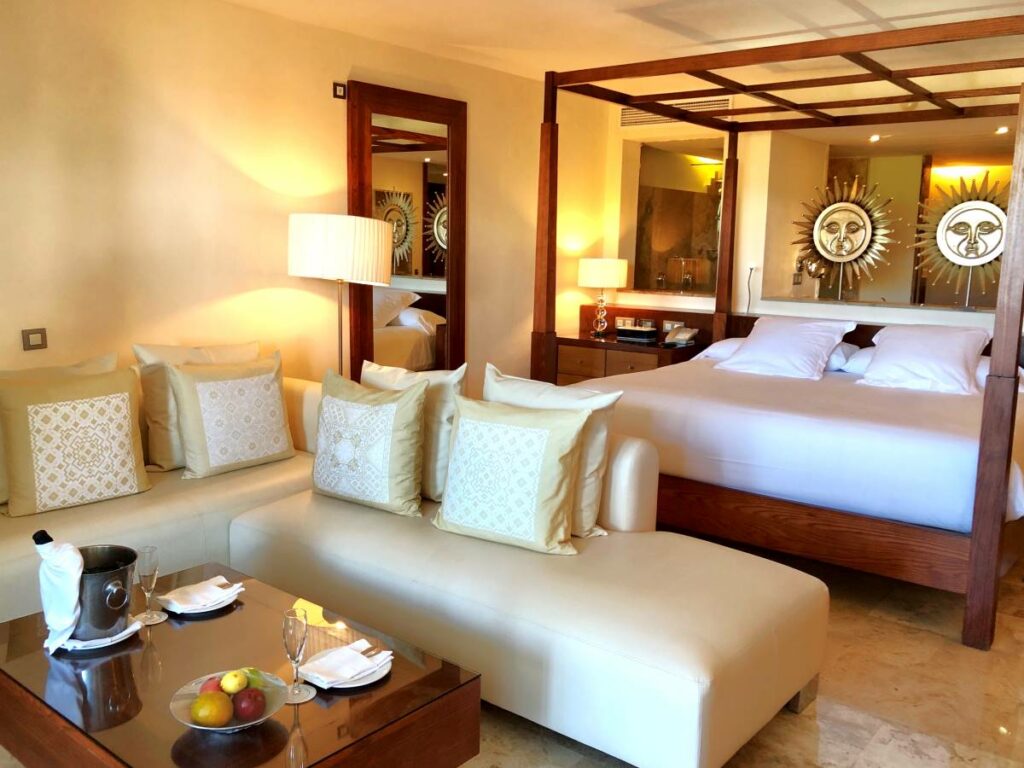 Elegant hotel suite with a king size bed, couches, a fruit bowl and wine bottle