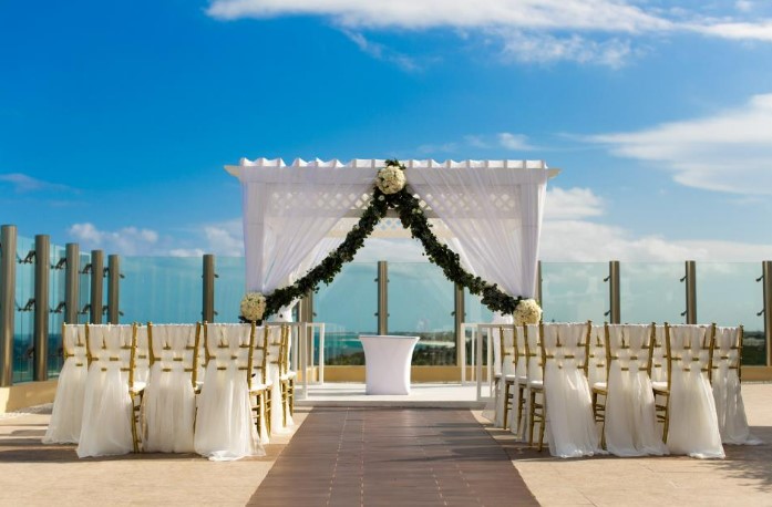 Wedding gazebo with green leaves and white flowers and gold chairs with white drapes