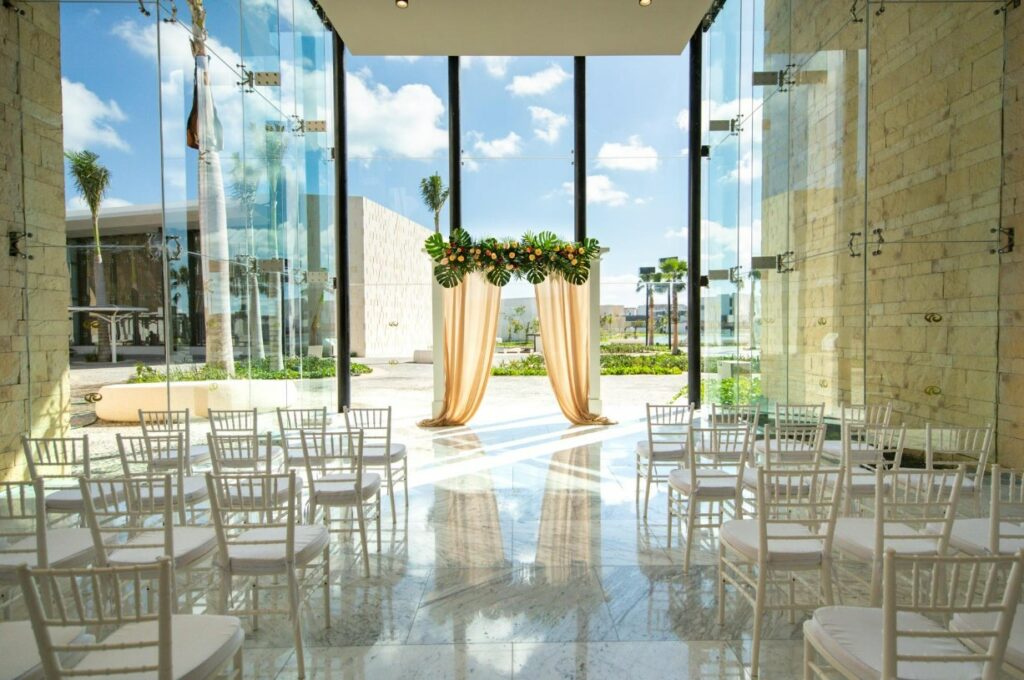 Wedding venue with large floor to ceiling windows and a pergola decorated with beige drapes and tropical leaves