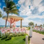 wedding gazebo overlooking the ocean with pink drapes and gold chairs with pink ribbons