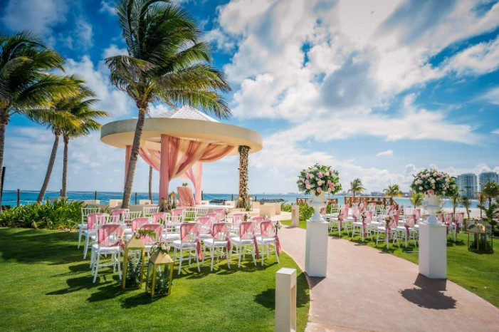 wedding gazebo overlooking the ocean with pink drapes and gold chairs with pink ribbons
