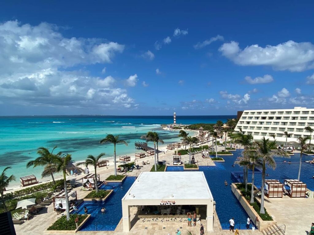Aerial view of the pool and beach area of a resort in Cancun with a lighthouse at the back