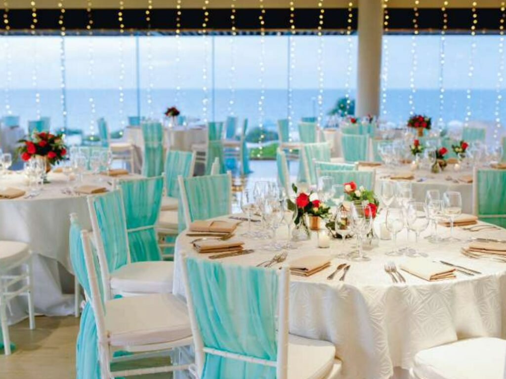 Wedding set up in a ballroom with ocean view, red tropical flowers and white chair drapes