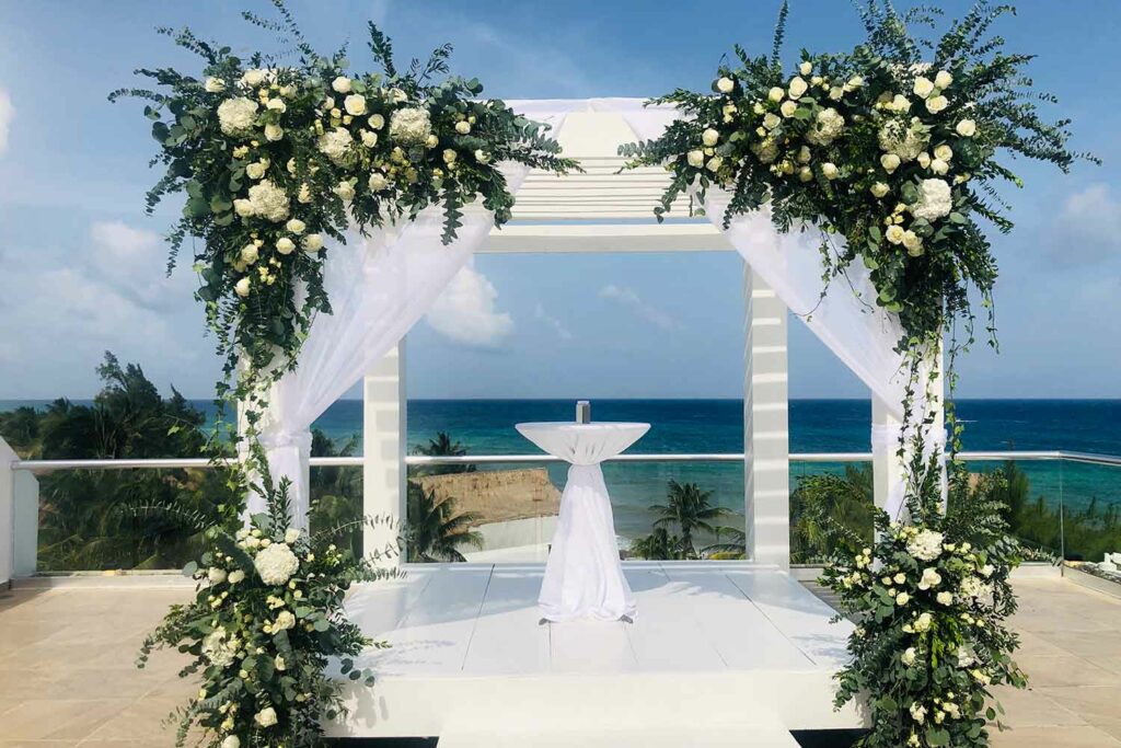 Wedding gazebo with white drapes and large flower arrangements with white flowers and green leaves
