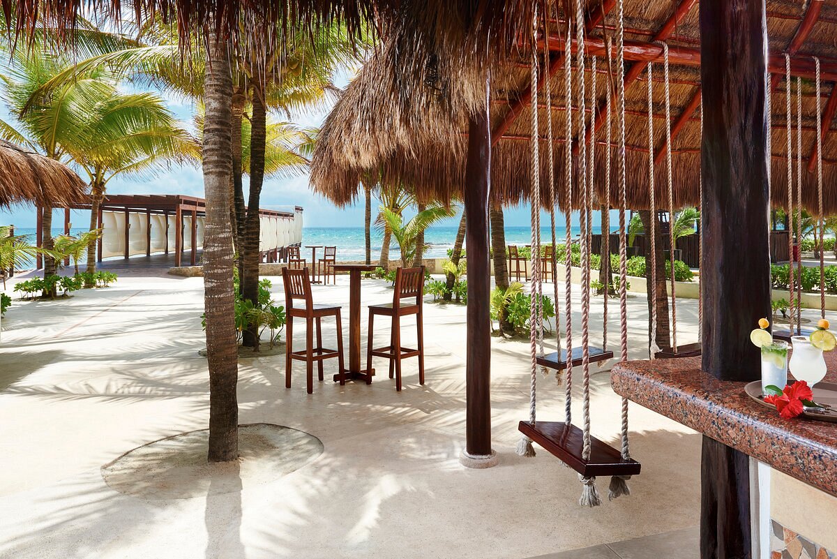 Beach bar in front of the sea and the wooden corridor, with wooden swings and high tables and chairs.