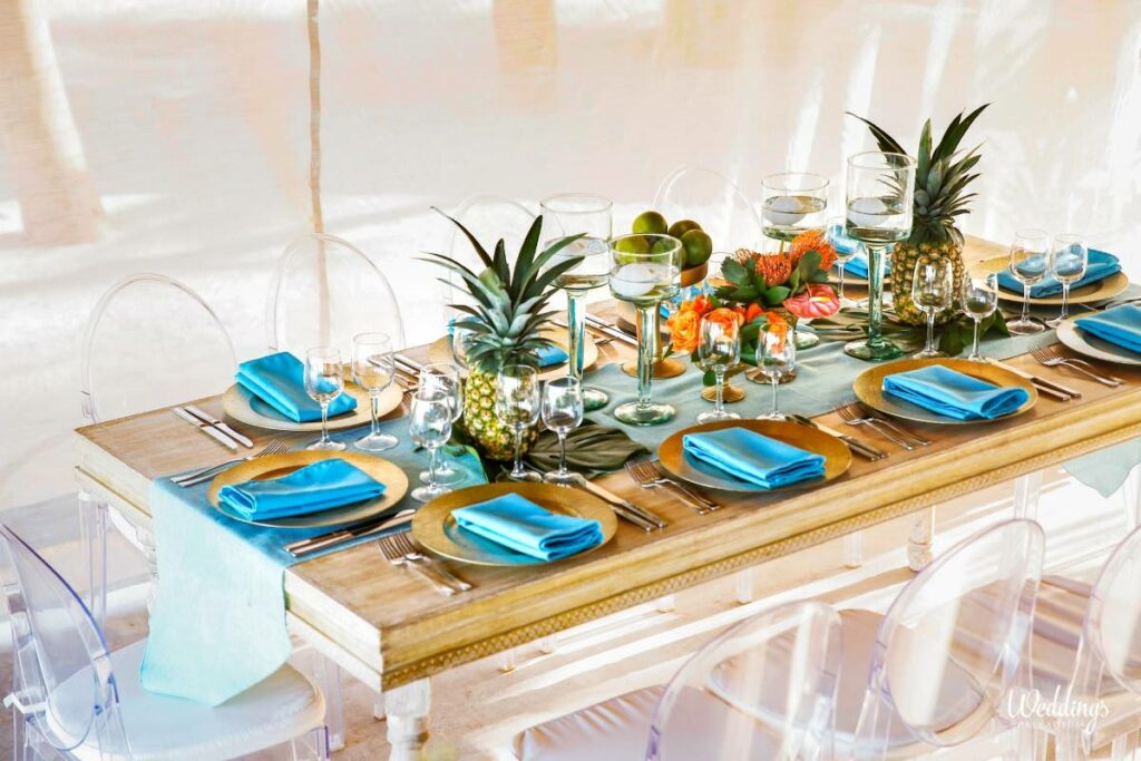 Wedding table decor with wood furniture, blue napkings and pineapples and tropical flowers