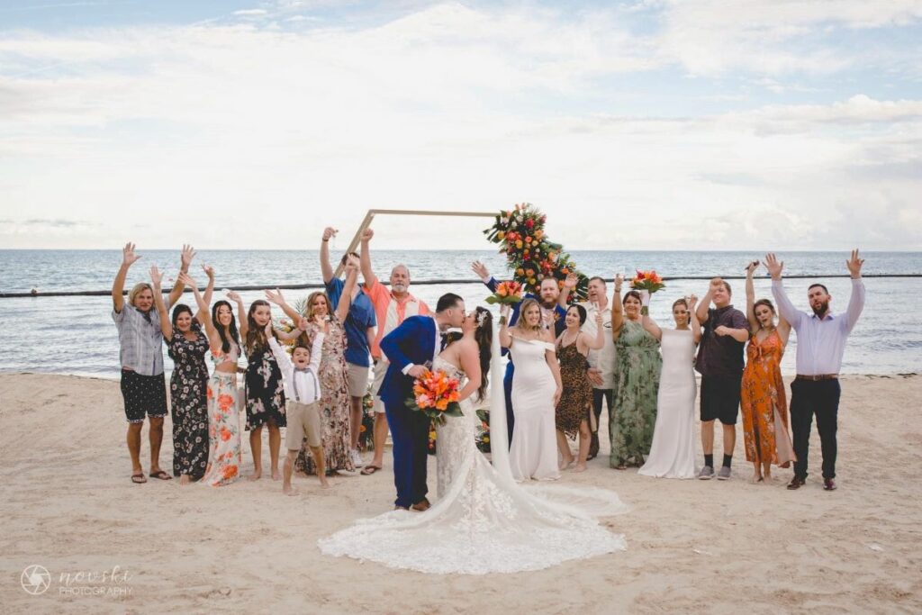 Just married couple kissing in front of their wedding group and the ocean front gazebo