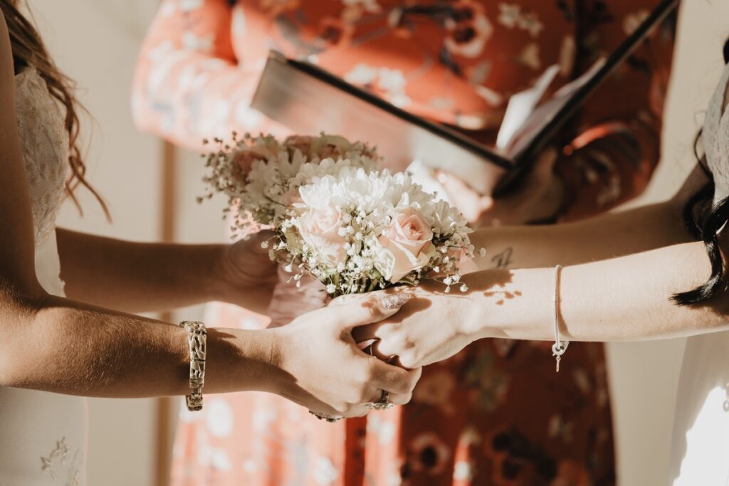 lesbian marriage ceremony with two women holding hands and flower bouquets