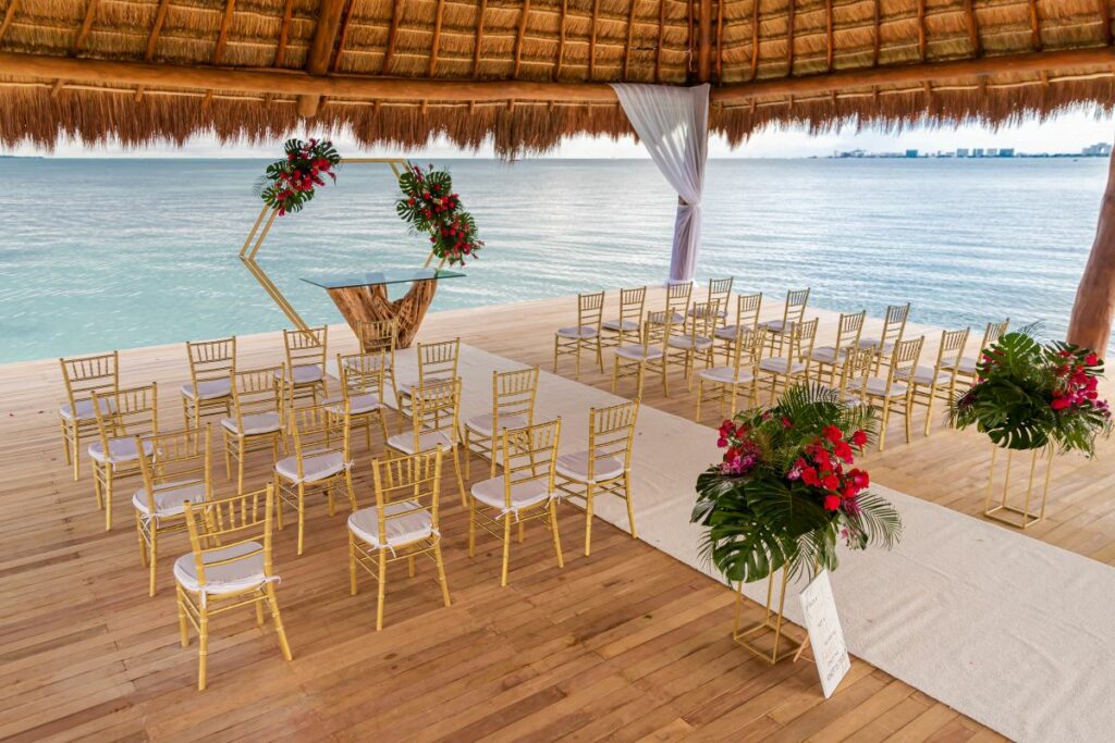 wedding set up in a palapa with ocean view, golden chairs and tropical flowers