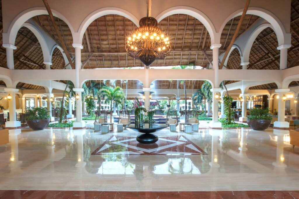 Open hotel lobby with large chandeliers and a big palapa roof with arches