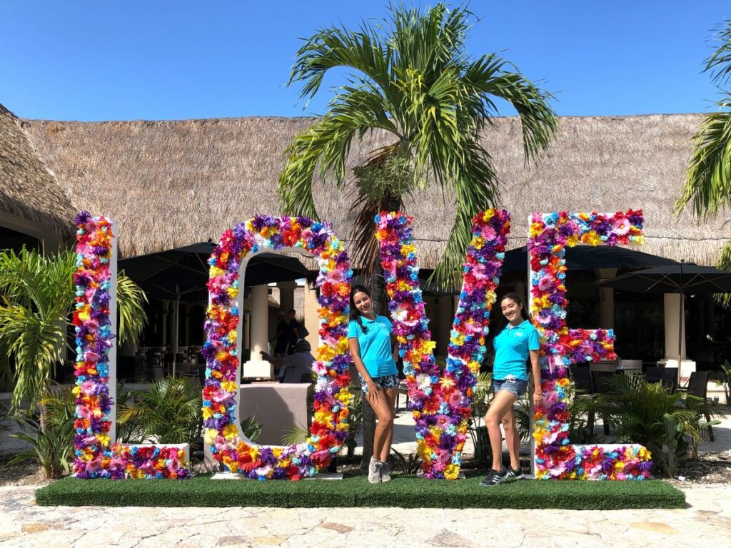Hola weddings staff posing on a large love letter sign with flowers