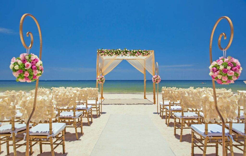 Beach set up with a gazebo and golden chairs with pink flowers