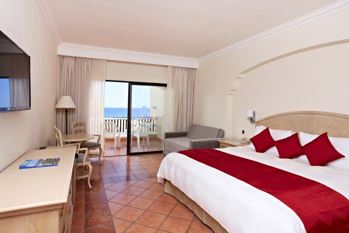 Hotel room with one king size bed with red cushions, a balcony with ocean view and sitting area