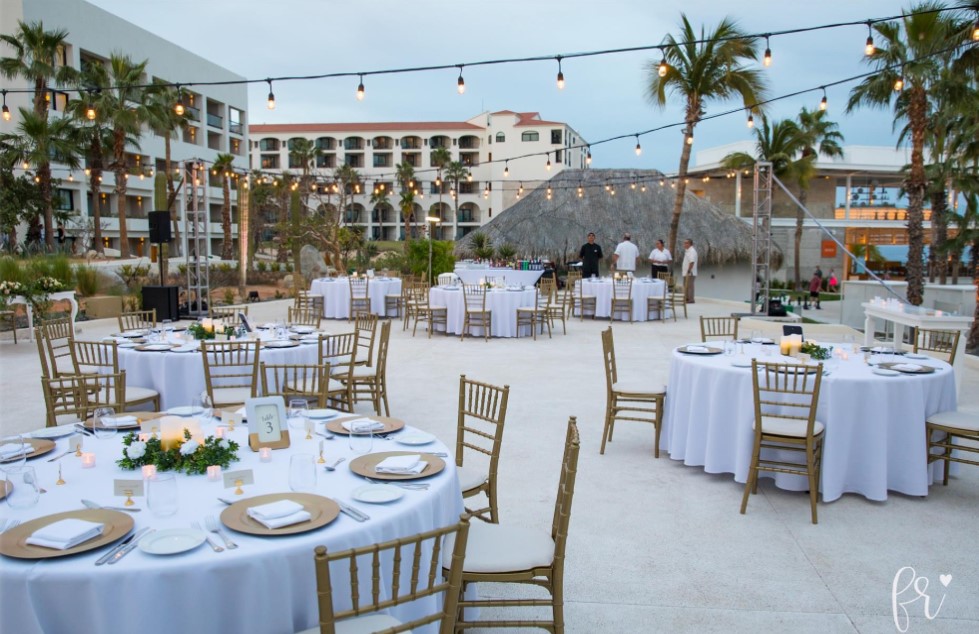 resort wedding venue with white tables and gold chairs surrounded by palm trees and resort building
