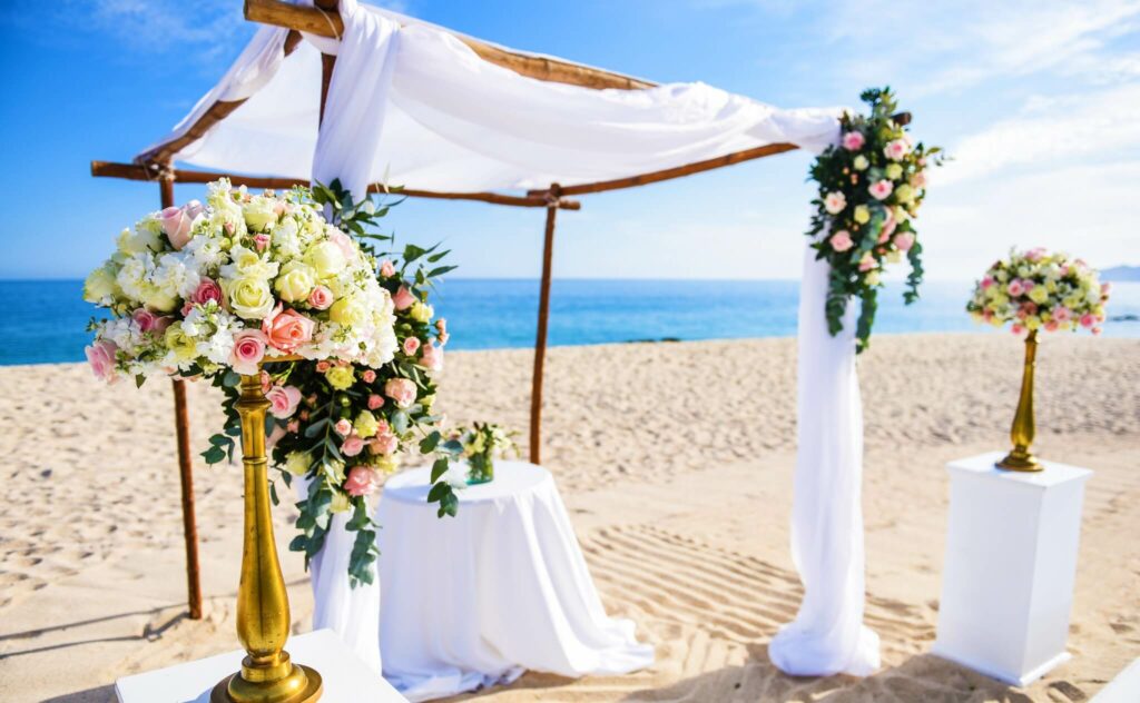 Beach wedding ceremony gazebo with white drapes and floral arrangements
