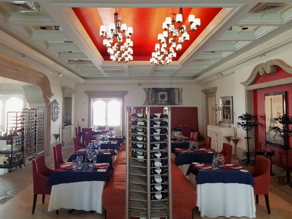 French restaurant with chandeliers, red chairs, blue table cloths and wine racks