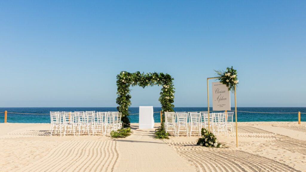 Cadre de cérémonie de mariage sur la plage avec une arche de fleurs et de verdure au dream los cabos wedding resort