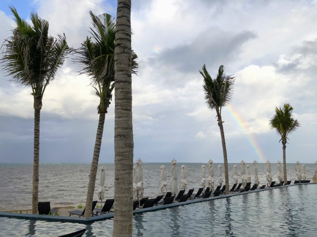 Infinity pool with lounge chairs, palm trees and a rainbow at the back