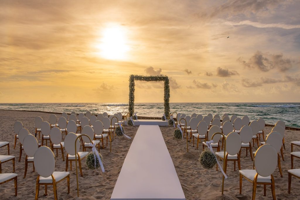 wedding at the beach with a sunset behind, with white and gold chairs