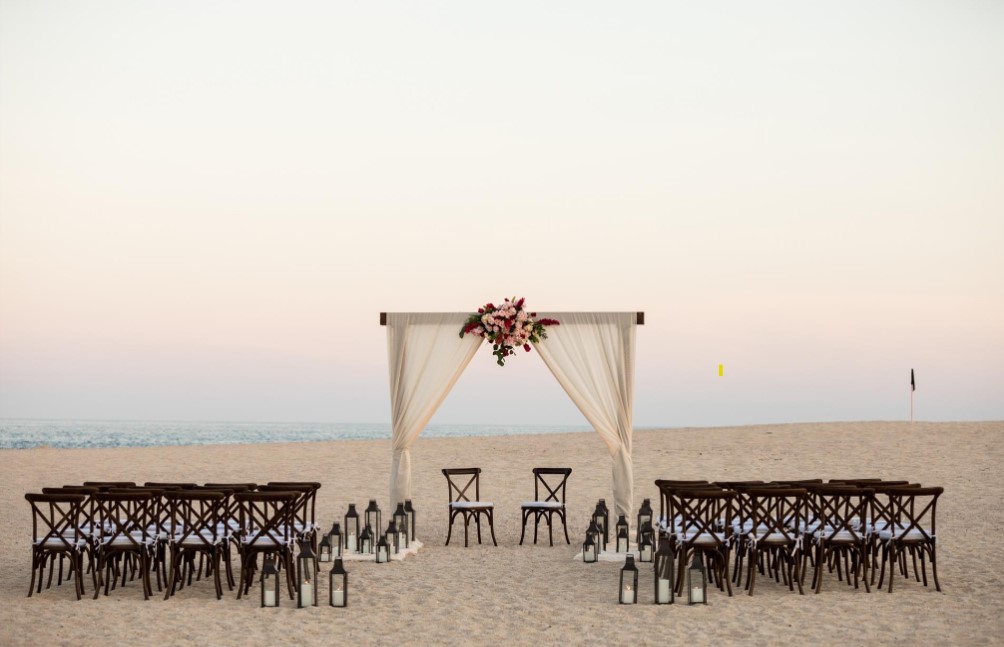 wedding at the beach shoe with a wedding arch and wooden chairs with a sunset on the background